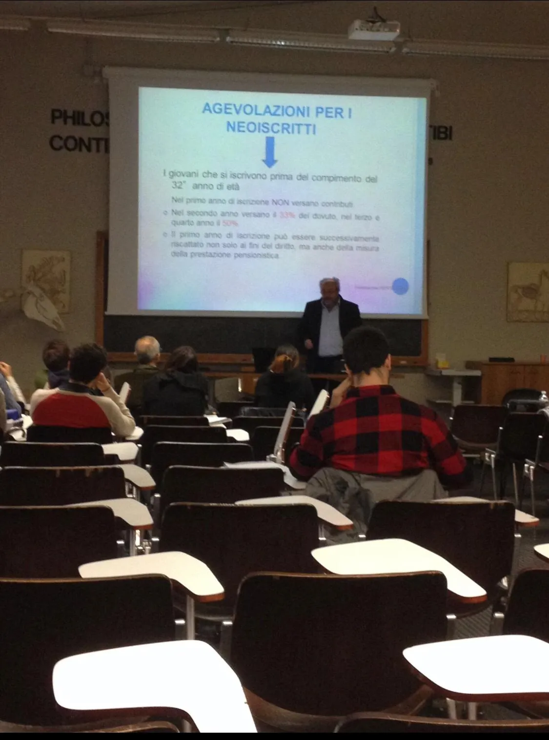 Un relatore in giacca scura davanti alla slide «Agevolazioni per i neoiscritti», in un’aula universitaria con banchi a ribalta.